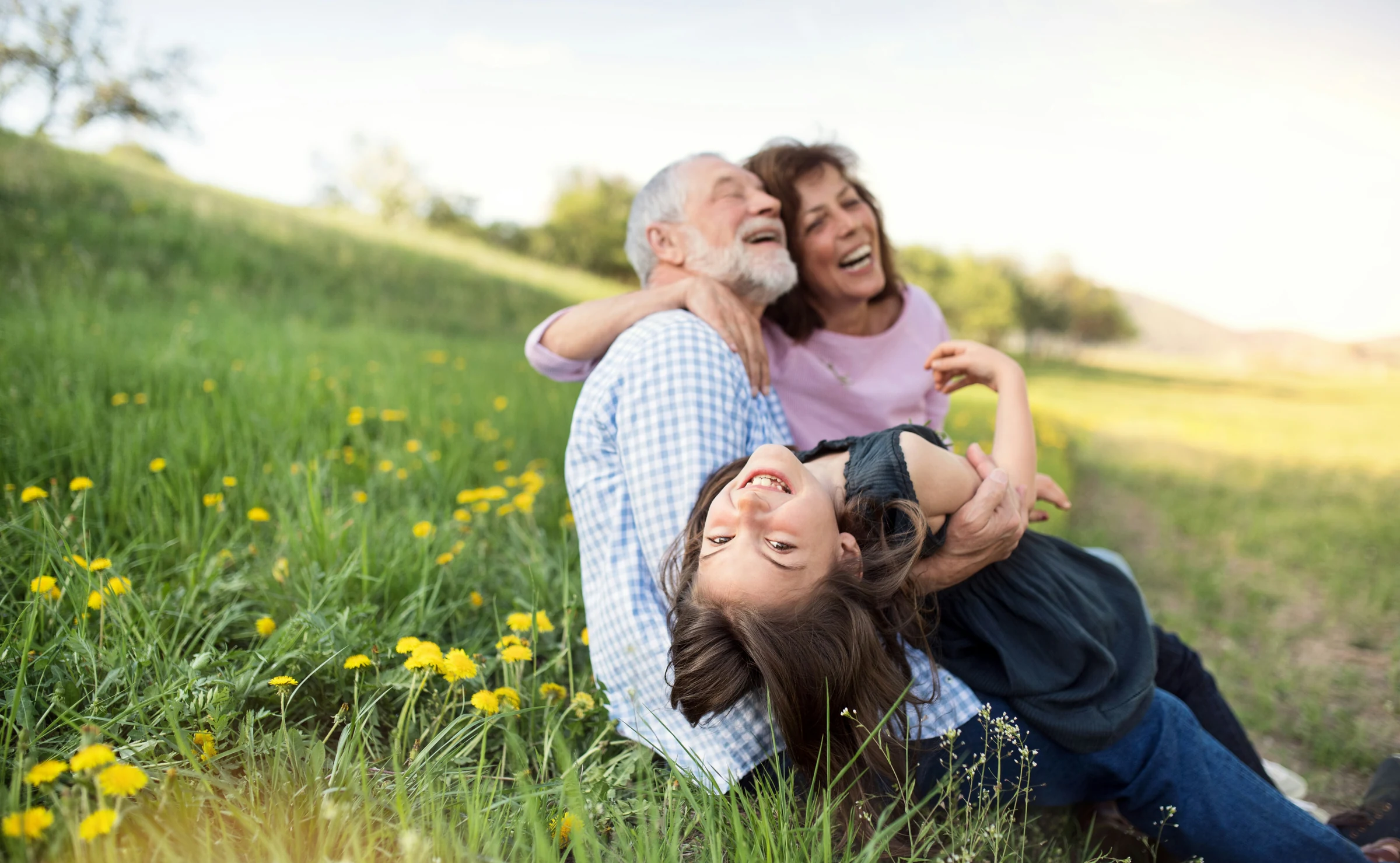 Grandparents playing with their granddaughter in a green field.