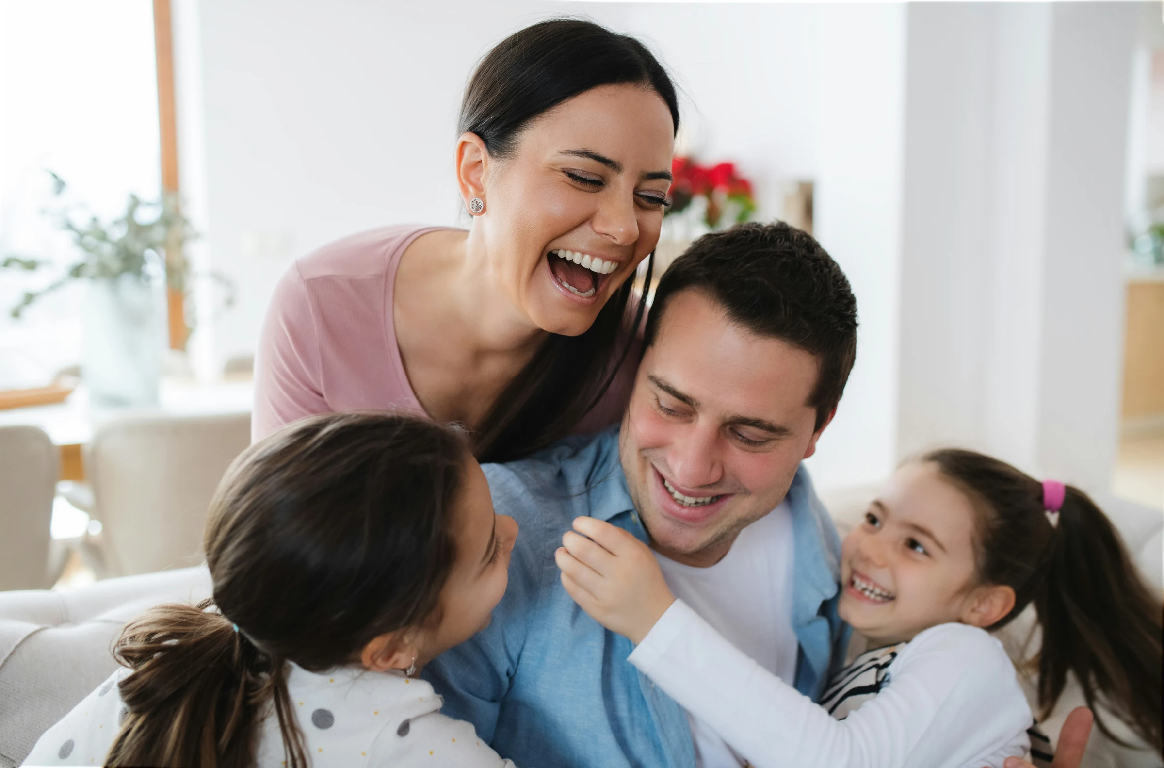 Parents and their two daughters laughing together on a sofa.
