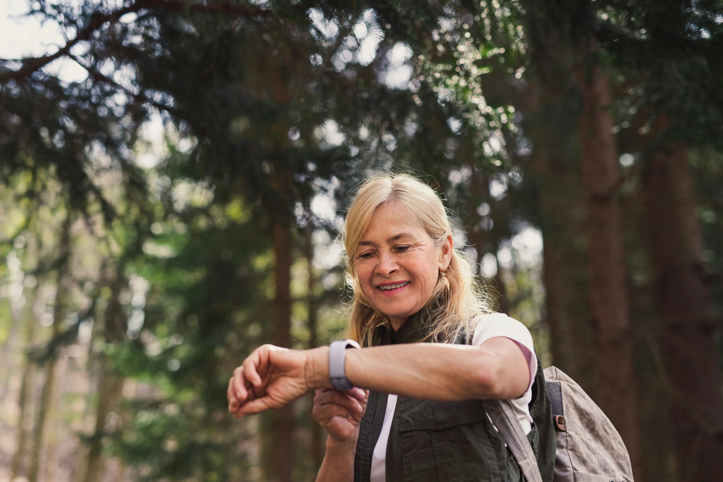 A woman checking her watch while walking in the woods.